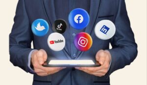 a photo of social media icons floating above a tablet in the hands of a man in a business suit