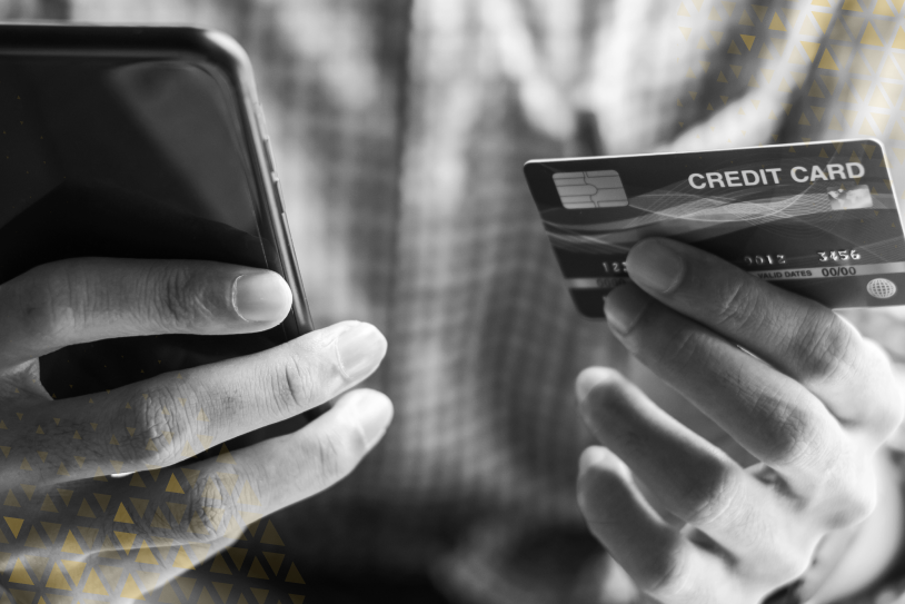 Man holding a credit card in one hand and a mobile phone in the other, entering payment details for an online transaction.