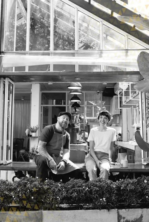 Man in apron and woman standing outside an open, airy café with concertina glass windows